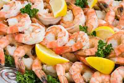 Pink Shrimp Cocktail on tray with lemon. Fresh peeled and cooked shrimp fanned out on tray with yellow lemon wedges and green parsley sprigs.