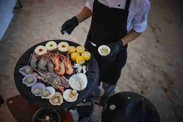 Chef preparing grilled crab, squid, and shrimp at an outdoor buffet.