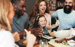 A joyful family sitting around the dinner table, enjoying a homemade meal, wine, and meaningful conversation in a cozy home setting.