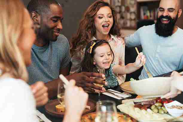 A joyful family sitting around the dinner table, enjoying a homemade meal, wine, and meaningful conversation in a cozy home setting.