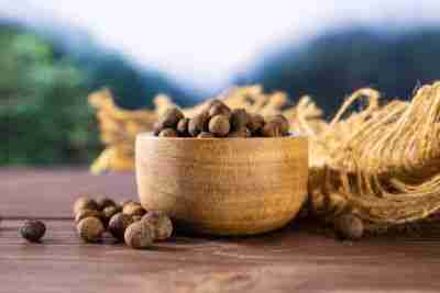 Lot of whole dry brown allspice berries with wooden bowl on jute cloth asian jungle in background