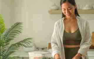 Young smiling sportswoman preparing containers with mixed vegetables for freezer.